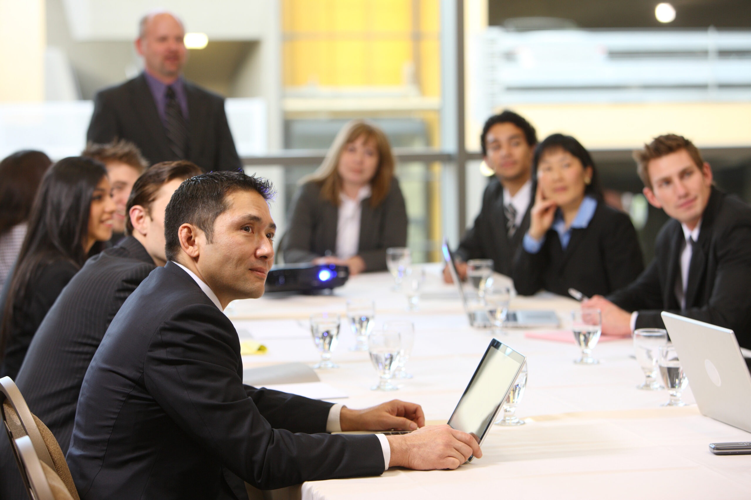 Business meeting with professionals engaged in discussion, featuring a speaker and attentive participants at a conference table.